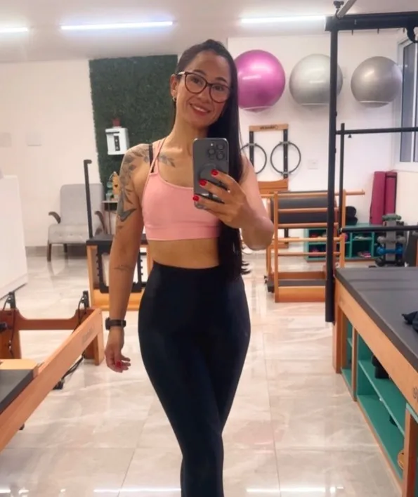 Denise Vendeirinho sorrindo no estúdio, com os aparelhos de Pilates ao fundo